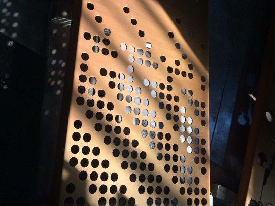 Perforated weathering steel sculpture panel lit by low angled sunlight